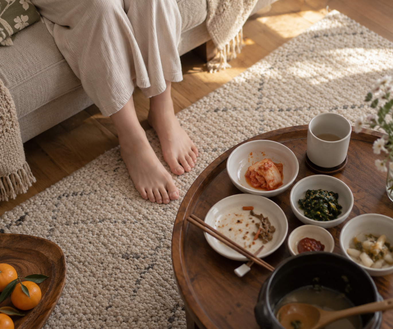 명절 상 옆 소파에서 맨발을 러그 위에 내려놓은 모습과 남은 반찬이 놓인 낮은 상을 위에서 내려다본 장면