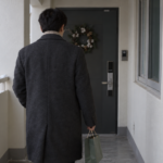 10월 눈 내린 아파트 복도에서 선물 가방을 들고 부모님 댁 현관으로 걸어가는 단정한 코트 차림의 뒷모습