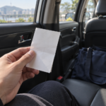 택시 뒷좌석에서 영수증 뒷면을 들고 남은 가방을 살피는 장면