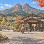 쌍봉 산을 배경으로 시골 역 광장을 걸어 나오는 여행자들의 일러스트